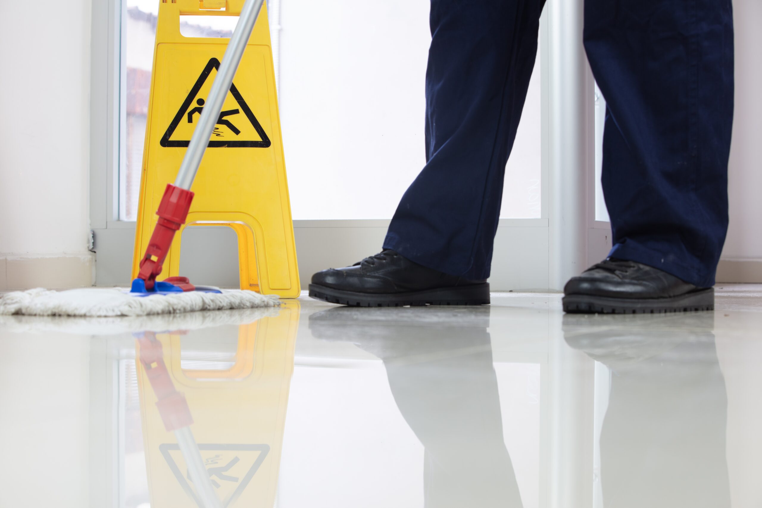 Services low angle closeup of a person cleaning the floor with a mop near a yellow caution wet floor sign